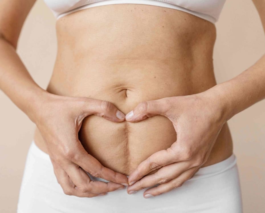 A woman making a heart shape with her hands on her stomach